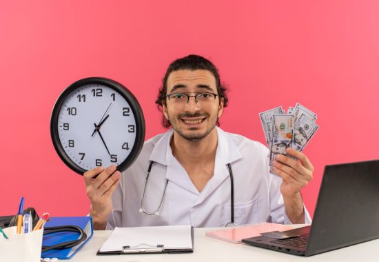 smiling-young-male-doctor-with-medical-glasses-wearing-medical-robe-with-stethoscope-sitting-desk